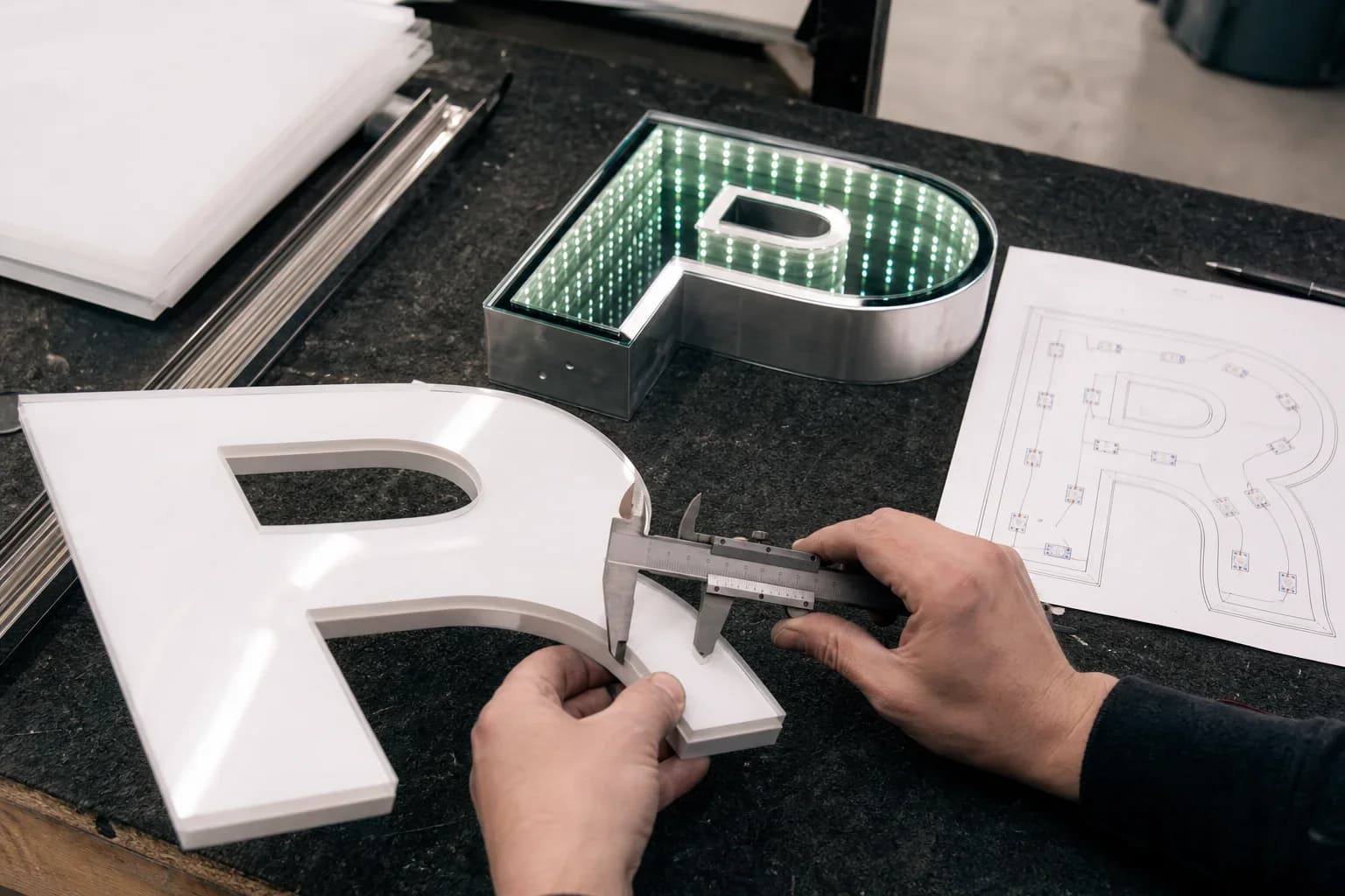 Fabricator measuring letter stroke width with calipers beside an assembled infinity mirror letter cell