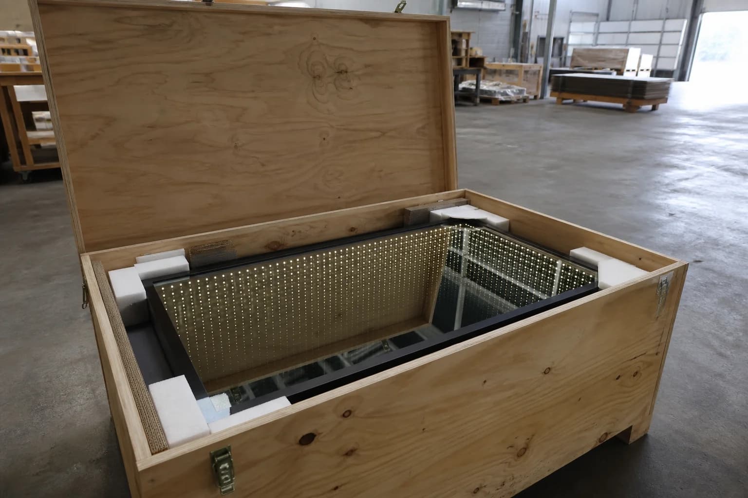 Open wooden export crate with foam corner blocks protecting a framed infinity mirror sign ready for overseas freight